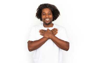 Moved African American man pressing hands to chest. Portrait of happy mature male model with dark curly hair in white T-shirt smiling, reacting to something cute. Kindness, sympathy concept - obrazy, fototapety, plakaty
