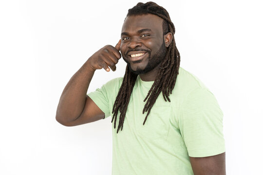 Smiling Black man showing phone call gesture at camera. Cheerful man with dreadlocks making call me gesture with hand while standing against white background. Communication concept