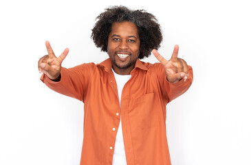 Portrait of happy mid adult man making victory gesture against white background. African American man wearing orange shirt showing peace gesture and smiling. Success and happiness concept