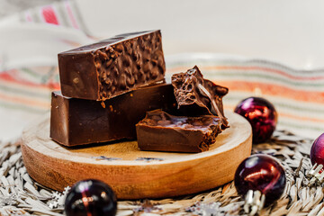 Christmas chocolate, rice and nut nougat on a wooden plate with a drape background and red - purple decoration balls