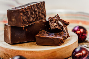 Chocolate, rice and nut Christmas nougat over a wooden plate on a white background with decorations