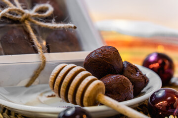 Christmas honey truffles on a white plate and a box on a wooden table with red decorations