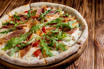 Pizza with jamon and prosciutto, mozzarella, cherry tomatoes, arugula and parmesan on a wood background. Italian cuisine.