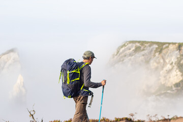 Obraz premium Side view of elderly man hiking on foggy day. Sportsman with backpack going uphill. Leisure, sport concept