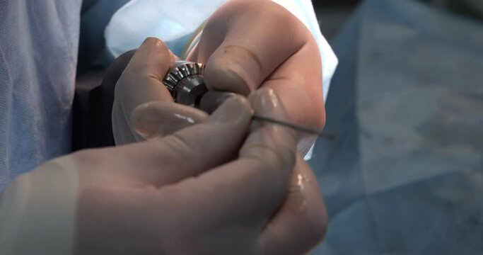 With a hand in a medical glove, the surgeon inserts the drill into the drill and secures it. The doctor performs an orthopedic operation by fixing the bones with bolts and a surgical drill.
