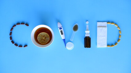 Covid word laid out of medications, pills, thermometer, traditional medicine for treating colds, flu, heat on a blue background. Maintenance of immunity. Seasonal diseases. Top view. Medicine flat lay