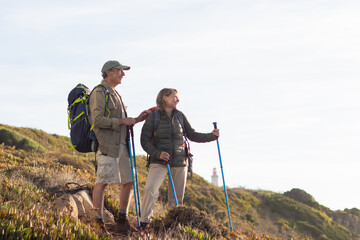 Happy elderly family hiking on summer. Man and woman in casual clothes and with ammunition looking...