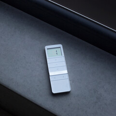 Remote control for window blinds. White remote control lying on a concrete windowsill near the...