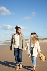 Front view of Caucasian couple on summer vacation. Bearded man and woman in casual clothes walking on beach, holding hands. Love, travelling, tenderness concept