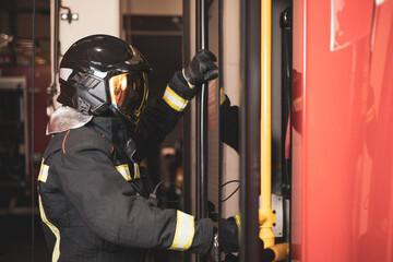 Fototapeta premium A firefighter dressed in uniform and with a helmet is about to get into the truck after being called for a fire, public service.