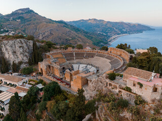 Fototapeta na wymiar Aerial view of the Ruins of the Ancient Greek Theater in Taormina, Sicily with the double smoke tail of the Etna extending over the the Giardini-Naxos bay of the Ionian Sea in the morning sun shine.