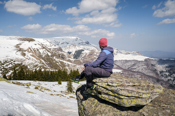 Mountain hiker sitting on the cliff covered by colorful moss looking at a distant snow covered peaks and landscape - 549315114