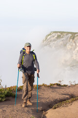 Obraz premium Portrait of mature hiker at mountain. Sportsman with backpack standing at cliff alone, looking at camera. Leisure, sport, hobby concept