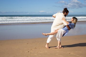 Joyful Caucasian couple dancing barefoot at the beach with fantastic sea view in background....