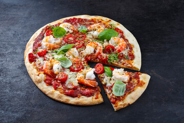 Traditionelle italienische Pizza frutti di mare Riesengarnelen, Tomaten und Mozzarella serviert als close-up auf einem rustikalen schwarzen Board 