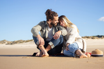 Content couple on summer vacation. Bearded man and woman in casual clothes sitting on blanket, leaning on shoulder, relaxing. Love, travelling, dating concept