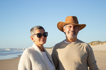 Portrait of lovely senior couple at seashore. Handsome grey-haired man in cowboy hat and short-haired woman in sunglasses spending vacation at seaside. Retirement, leisure concept