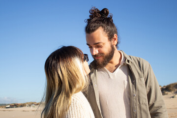 Warm couple walking on beach. Bearded man and woman in glasses looking at each other with love. Love, vacation, affection concept