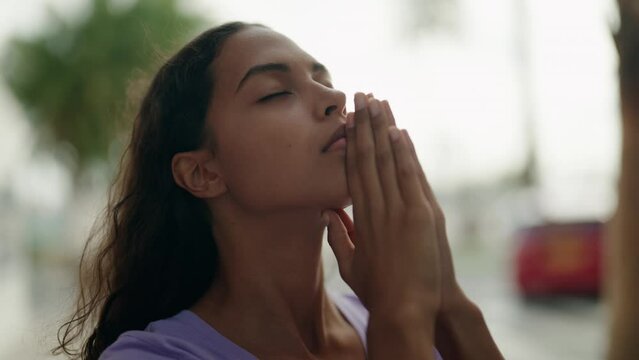 Young african american woman praying with closed eyes at street
