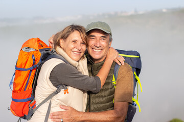 Portrait of fond elderly hikers. Man and woman with backpacks looking at landscape, hugging....