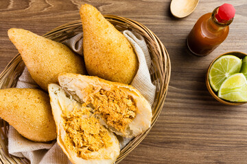 Chicken Coxinha, known as Coxinha in Brazil. Served in the basket, with spices such as lemon and pepper on the side. Wooden table in the background. Traditional brazilian snack Selective focus