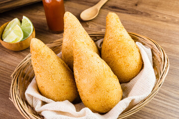 Chicken Coxinha, known as Coxinha in Brazil. Served in the basket, with spices such as lemon and pepper on the side. Wooden table in the background. Traditional brazilian snack Selective focus