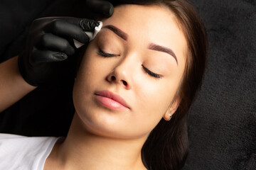 Tattoo master finishing permanent tattoo work, cleaning brows with a cotton pad