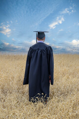 graduate student wearing gown in field day sky looking to future