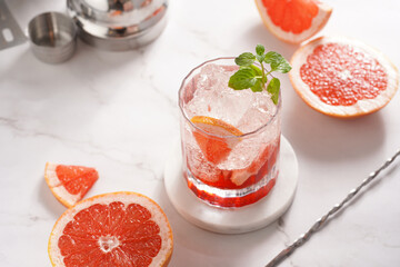 Preparation of a grapefruit alcohol free cocktail - A tumbler glass with ice cubes on marble...