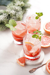 Preparation of a grapefruit alcohol free cocktail - several tumbler glasses with ice cubes on marble surface with fresh mint , christmas decoration