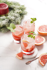 Preparation of a grapefruit alcohol free cocktail - several tumbler glasses with ice cubes on marble surface with fresh mint , christmas decoration
