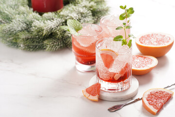 Preparation of a grapefruit alcohol free cocktail - several tumbler glasses with ice cubes on marble surface with fresh mint , christmas decoration