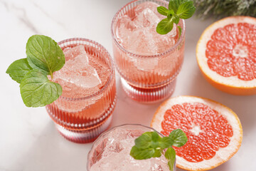 Preparation of a grapefruit alcohol free cocktail - several tumbler glasses with ice cubes on marble surface with fresh mint