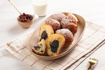 Several deep fried sweet balls made of yeast dough - donuts with poppy and cherry filling on an oval off-white plate on a checkered kitchen towel. unhealthy dessert