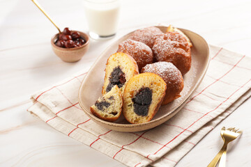 Several deep fried sweet balls made of yeast dough - donuts with poppy and cherry filling on an oval off-white plate on a checkered kitchen towel. unhealthy dessert