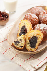 Several deep fried sweet balls made of yeast dough - donuts with poppy and cherry filling on an oval off-white plate on a checkered kitchen towel. unhealthy dessert
