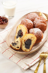 Several deep fried sweet balls made of yeast dough - donuts with poppy and cherry filling on an oval off-white plate on a checkered kitchen towel. unhealthy dessert