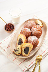 Several deep fried sweet balls made of yeast dough - donuts with poppy and cherry filling on an oval off-white plate on a checkered kitchen towel. unhealthy dessert
