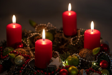 Obraz na płótnie Canvas Advent and Christmas lights, four red candles on a wreath with decoration against a dark background, copy space, selected focus