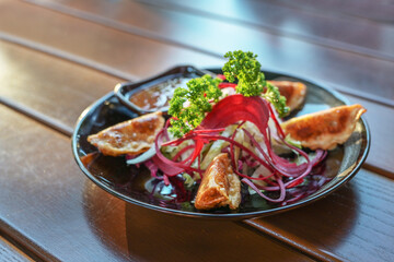 Deep fried gyoza with salad and sauce served as appetizer on a black plate, Asian dish on a wooden table, copy space, selected focus