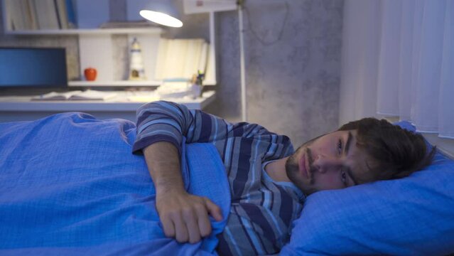 The young man who has trouble sleeping cant sleep.
Young man in bed having trouble sleeping at night.
