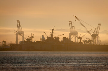Cranes and Dry Dock Lifts in Elliott Bay, Seattle, Washington During a Beautiful Sunrise. Industrial shipping and heavy equipment are silhouetted on a foggy morning in the Pacific Northwest.