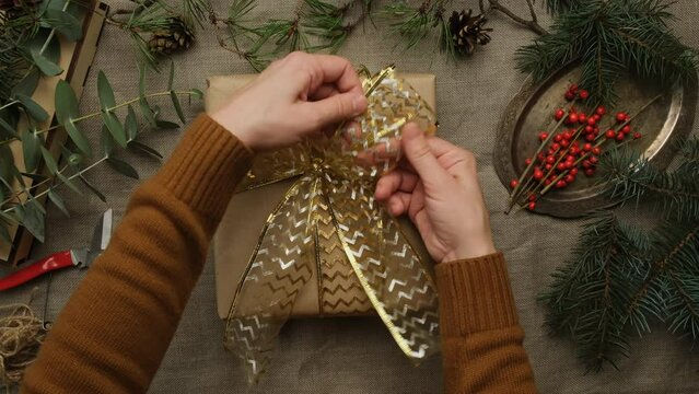 Hands tie a gift wrapping bow. Woman decorating Christmas gift box.