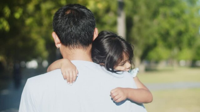 Rear view of Asian father carrying his sleeping little daughter. Cute tired girl napping on shoulder of her dad. Fatherhood concept