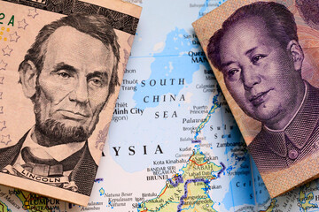 A US dollar bill and a yuan Chinese banknote on top of a map showing the South China Sea
