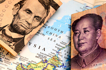 A US dollar bill and a yuan Chinese banknote on top of a map showing the South China Sea - 549332927