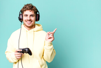 young adult caucasian man smiling cheerfully, feeling happy and pointing to the side with headset and a controller. gamer concept © kues1