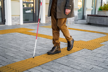 Blind man with a walking stick. Walks on tactile tiles for self-orientation while moving through the streets of the city
