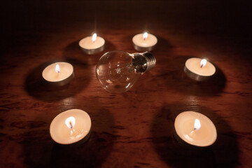 Power outage concept. Non-burning electric light bulb in a circle of burning candles