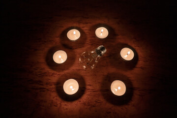 Power outage concept. Non-burning electric light bulb in a circle of burning candles